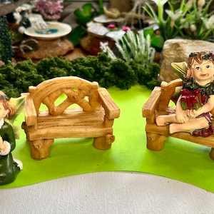 May include: Two miniature wooden benches with intricate details, one with a fairy figurine sitting on it. The fairy is wearing a green dress and has green wings. The benches are brown and have a rustic look.