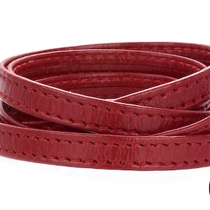 Peut inclure: Cordon en cuir rouge avec surpiqûres, enroulé. Le cordon est fabriqué aux États-Unis par All California Leather Supplies depuis 2013.