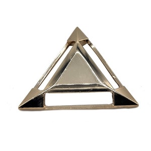 Op de afbeelding: Een gouden driehoekige hanger met een geometrisch ontwerp. De hanger heeft een holle kern en is gemaakt van metaal.