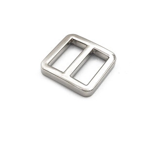 May include: A shiny, silver-colored metal slider buckle with a rectangular shape and two parallel bars. The buckle is designed for use in various crafting and sewing projects, such as bags and straps.
