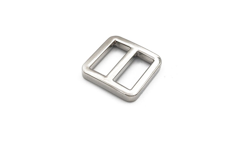 May include: A shiny, silver-colored metal slider buckle with a rectangular shape and two parallel bars. The buckle is designed for use in various crafting and sewing projects, such as bags and straps.