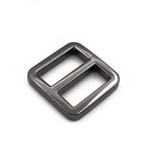 May include: A dark gray metal slider buckle with a rectangular shape and two openings. The buckle is made of a shiny metal and is set against a white background. This hardware component is used in various crafting projects.
