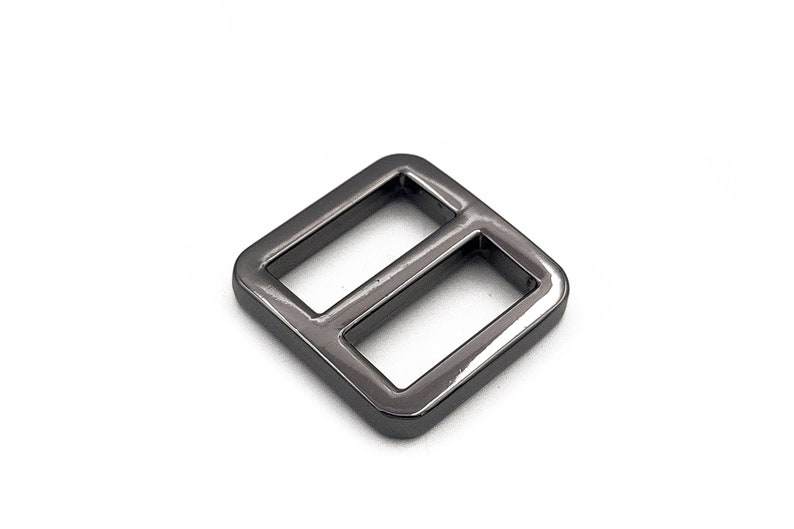 May include: A dark gray metal slider buckle with a rectangular shape and two openings. The buckle is made of a shiny metal and is set against a white background. This hardware component is used in various crafting projects.