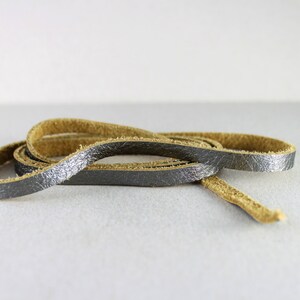 May include: A close-up of a length of brown leather cord with a silver metallic finish. The cord is coiled and ready for use in crafting projects.