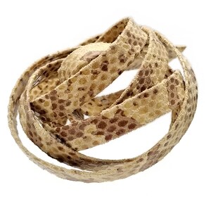 Puede incluir: Un cordón de cuero beige con un patrón de piel de serpiente marrón. El cordón está enrollado y listo para ser utilizado en proyectos de artesanía.