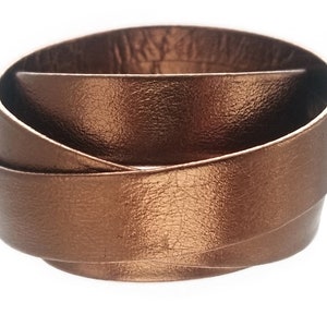 May include: A copper-coloured leather bracelet with a braided design. The bracelet is made of three strands of leather that are woven together.