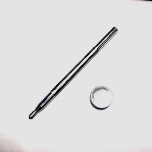 May include: A silver metal tool with a textured handle and a small, round cap. The tool has a pointed end and a cylindrical body. The cap is also silver and has a smooth, reflective surface. The items are on a white surface.