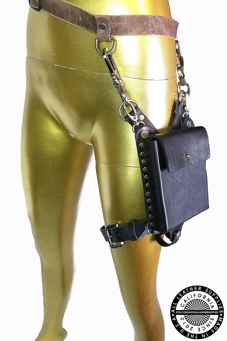 May include: Black leather thigh holster with a small pocket and a chain connecting to a belt. The holster is decorated with silver studs and has a buckle closure.