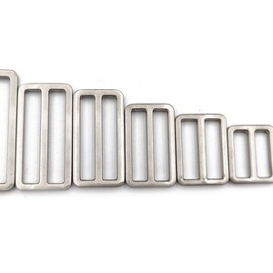 May include: A collection of seven silver-colored rectangular metal slides, each with three slots. The slides vary in size, arranged from largest to smallest, suitable for various crafting and sewing projects. They are displayed against a white background.