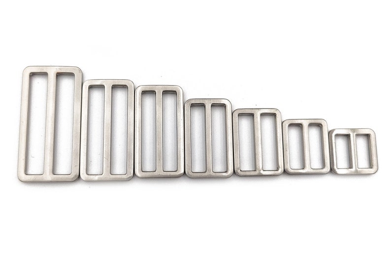 May include: A collection of seven silver-colored rectangular metal slides, each with three slots. The slides vary in size, arranged from largest to smallest, suitable for various crafting and sewing projects. They are displayed against a white background.