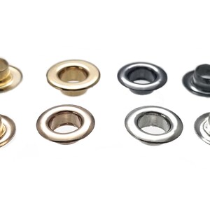 May include: Assortment of eight metal eyelets in various finishes, including gold, silver, and black. The eyelets are arranged in two rows of four.
