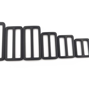 May include: A collection of black rectangular tri-glide slides in various sizes. Each slide has three vertical slots. The slides are arranged from largest to smallest, showcasing a range of dimensions for various applications.