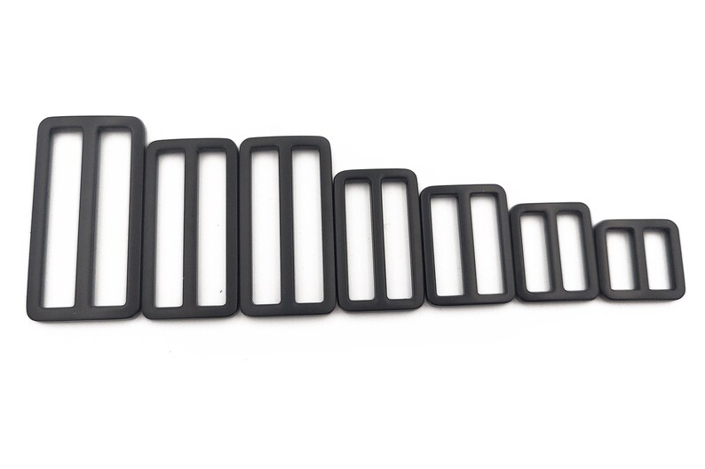 May include: A collection of black rectangular tri-glide slides in various sizes. Each slide has three vertical slots. The slides are arranged from largest to smallest, showcasing a range of dimensions for various applications.
