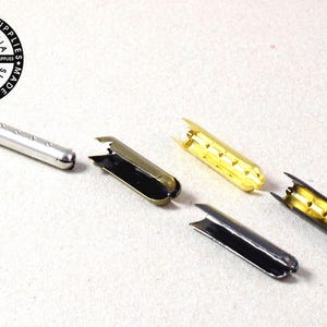 May include: A selection of metal cord ends in silver, gold, and black. One end is attached to a black cord. The image includes the text "ALL LEATHER SUPPLIES CALIFORNIA" and "MADE IN THE U.S.A."