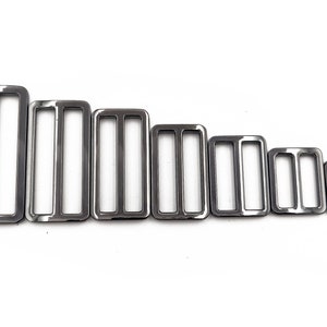 May include: A collection of seven silver-colored rectangular metal slides, each with two interior bars. The slides are arranged in descending order by size, from largest to smallest, against a white background. These are likely used for straps or belts.