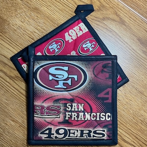 May include: Two red and black pot holders with the San Francisco 49ers logo and the text "49ers" and "San Francisco".