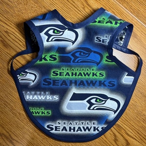 May include: A blue, green, and white dog vest with the Seattle Seahawks logo and text repeated throughout the fabric.
