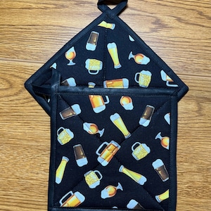May include: A pair of black quilted pot holders with a beer-themed print. The pot holders have a hanging loop and are made of a quilted fabric with a black background and a pattern of beer mugs, glasses, and bottles.