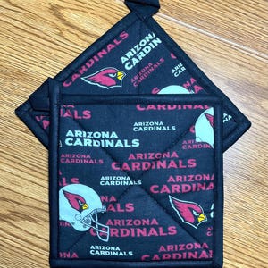 May include: Two black and red Arizona Cardinals pot holders with a quilted design. The pot holders feature the team logo and the words "Arizona Cardinals".