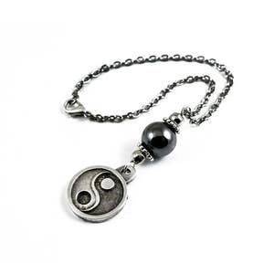 Könnte beinhalten: Eine silberne Kettenkette mit einer schwarzen Perle und einem silbernen Anhänger mit einem Yin-Yang-Symbol.