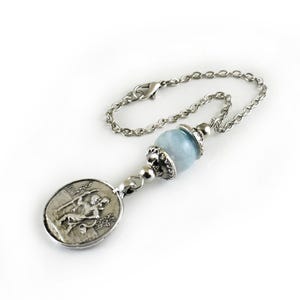 Puede incluir: Una pulsera de cadena de metal plateado con una cuenta de piedra preciosa azul claro acentuada con tapas plateadas ornamentadas y un colgante circular que representa en relieve una figura sentada. Incluye un cierre de mosquet&oacute;n.