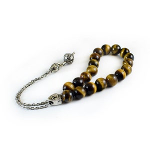 K&ouml;nnte beinhalten: Eine braune und goldene Tigerauge-Perlenmala mit silbernen Akzenten. Die Mala ist auf einer silbernen Kette mit einem Quaste aufgef&auml;delt.