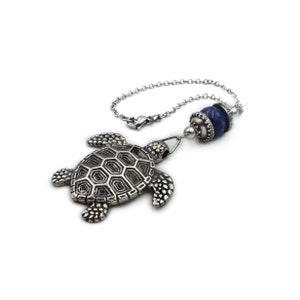 Könnte beinhalten: Ein silberner Schildkrötenanhänger mit einer blauen Lapislazuli-Perle und einer silbernen Kette.