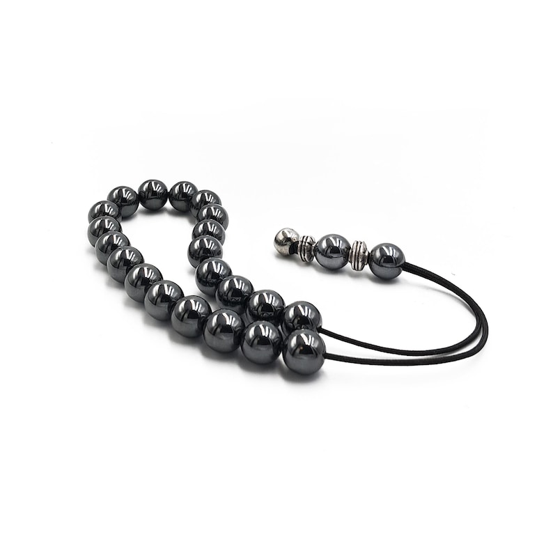 Puede incluir: Un collar de cuentas de oraci&oacute;n mala de hematita negra con un cord&oacute;n negro y detalles plateados.