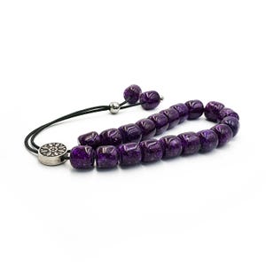 May include: A purple prayer beads necklace with a silver charm. The beads are made of glass and have a speckled finish.