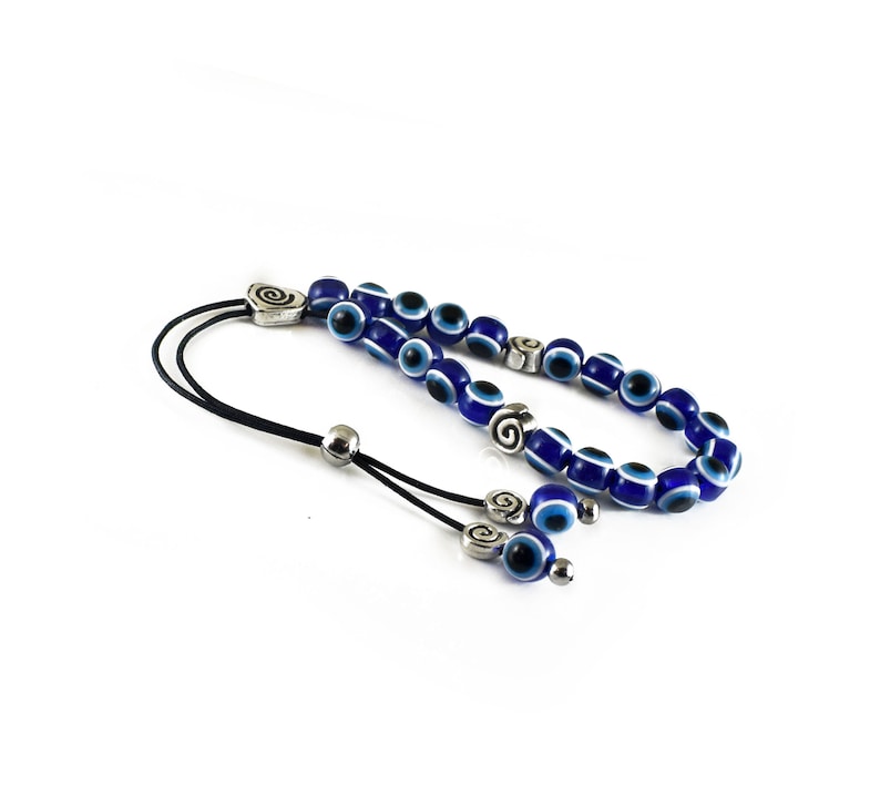 May include: A blue and white evil eye bead necklace with silver accents. The necklace is made of small round beads with a blue background and a white eye design. The necklace has a silver clasp and a silver charm with a spiral design.