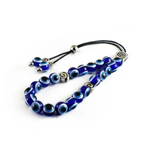 May include: A blue and white evil eye bead necklace with silver accents. The necklace is made of glass beads and has a black cord.