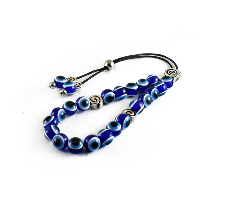 May include: A blue and white evil eye bead necklace with silver accents. The necklace is made of glass beads and has a black cord.