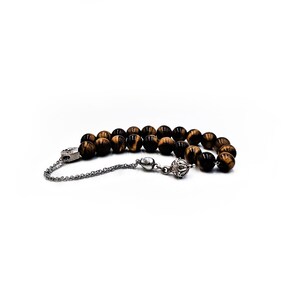 K&ouml;nnte beinhalten: Eine braune und schwarze Tigerauge-Perlenmala mit einem silbernen Quaste und einem silbernen Anh&auml;nger.