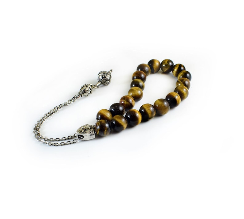 K&ouml;nnte beinhalten: Eine braune und goldene Tigerauge-Perlenmala mit silbernen Akzenten. Die Mala ist auf einer silbernen Kette mit einem Quaste aufgef&auml;delt.