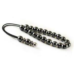 Puede incluir: Un collar de cuentas de hematites negras con un acento de cuentas plateadas. El collar est&aacute; encordado en un cord&oacute;n negro.