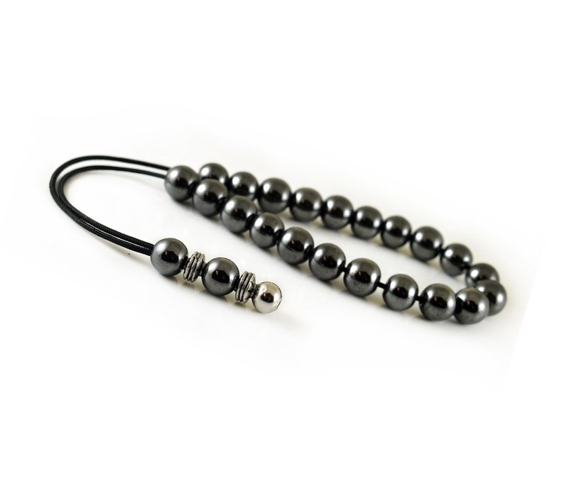 Puede incluir: Un collar de cuentas de hematites negras con un acento de cuentas plateadas. El collar est&aacute; encordado en un cord&oacute;n negro.