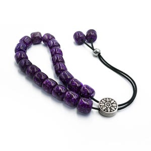 May include: A purple prayer bead mala with a silver tassel and a silver charm with a floral design.