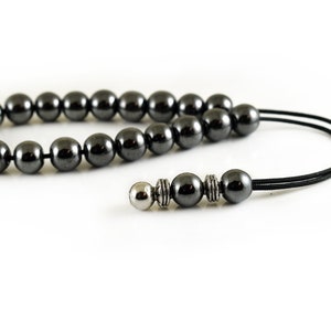 Puede incluir: Un collar de cuentas de hematites negras con una cuenta de acento plateada y un cord&oacute;n negro.