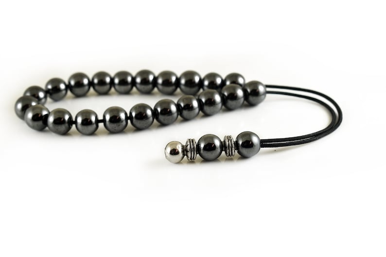 Puede incluir: Un collar de cuentas de hematites negras con una cuenta de acento plateada y un cord&oacute;n negro.