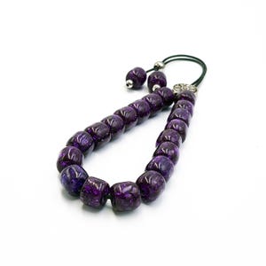 May include: A purple prayer beads mala with a silver tassel and a silver charm. The beads are made of a translucent material with a speckled pattern.