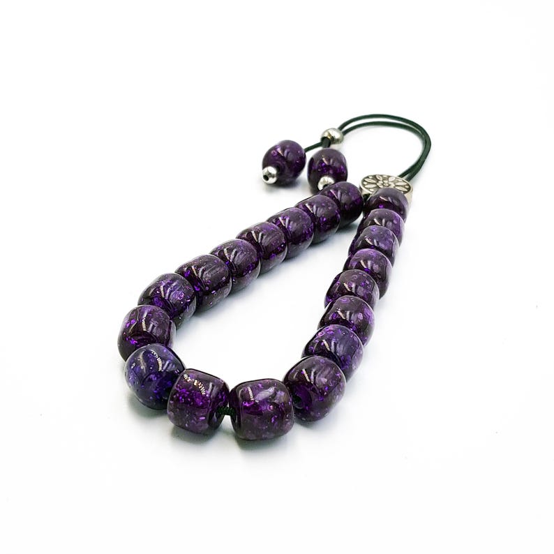 May include: A purple prayer beads mala with a silver tassel and a silver charm. The beads are made of a translucent material with a speckled pattern.