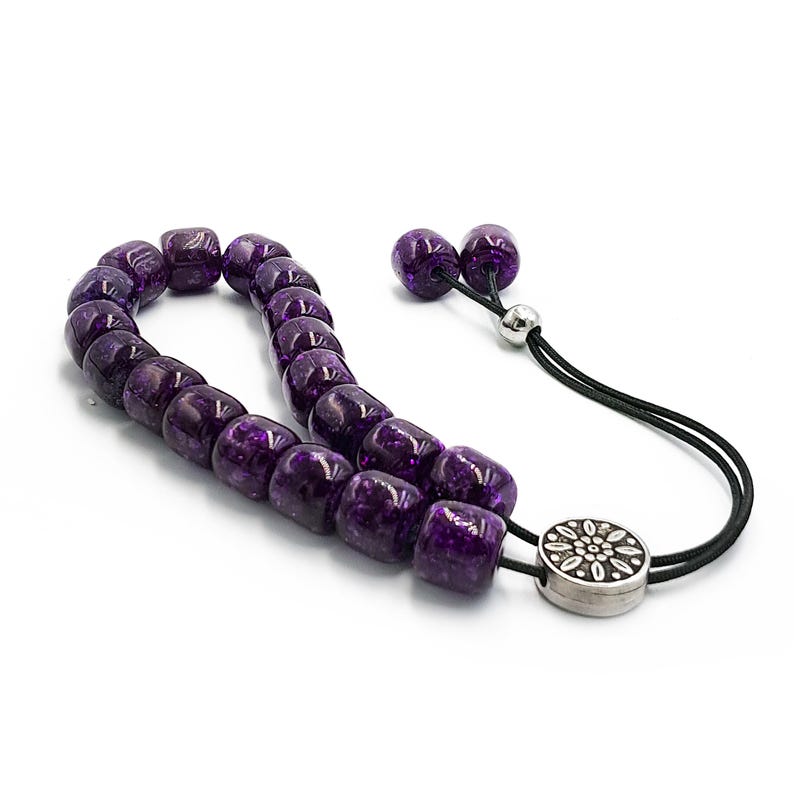 May include: A purple prayer beads mala with a silver tassel and a silver charm. The beads are made of glass and have a speckled finish.