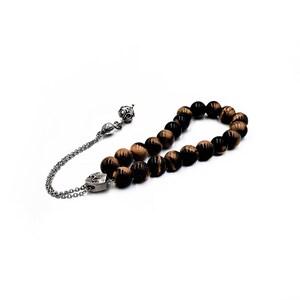 K&ouml;nnte beinhalten: Eine braune und schwarze Tigerauge-Perlenmala mit einem silbernen Anh&auml;nger und einer silbernen Kette.