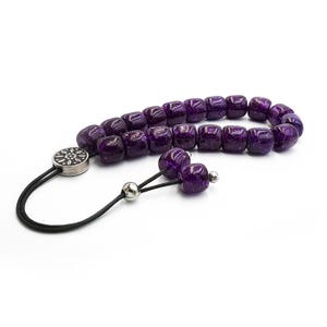 May include: A purple prayer beads necklace with a silver tassel and a silver charm. The beads are made of glass and have a sparkly finish.