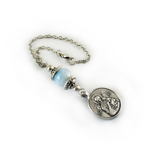 Puede incluir: Una cadena de metal plateado con una cuenta de piedra esf&eacute;rica de color azul claro, acentuada por tapas decorativas plateadas. En el extremo de la cadena hay un colgante de metal plateado de forma ovalada que representa una figura religiosa.