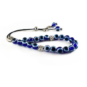 May include: A blue evil eye bead bracelet with silver charms. The bracelet is made of small, round beads with a white centre and a blue outer ring. The charms are silver and have a spiral design.