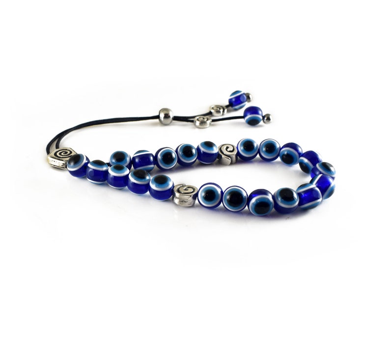 May include: A blue evil eye bead bracelet with silver charms. The bracelet is made of small, round beads with a white centre and a blue outer ring. The charms are silver and have a spiral design.