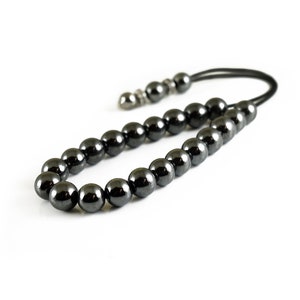 Puede incluir: Un collar de cuentas de hematites negras con un cierre plateado y un cord&oacute;n negro.