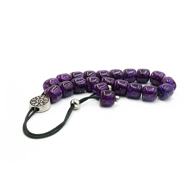 May include: A purple prayer beads necklace with a silver charm. The beads are made of glass and have a speckled finish.