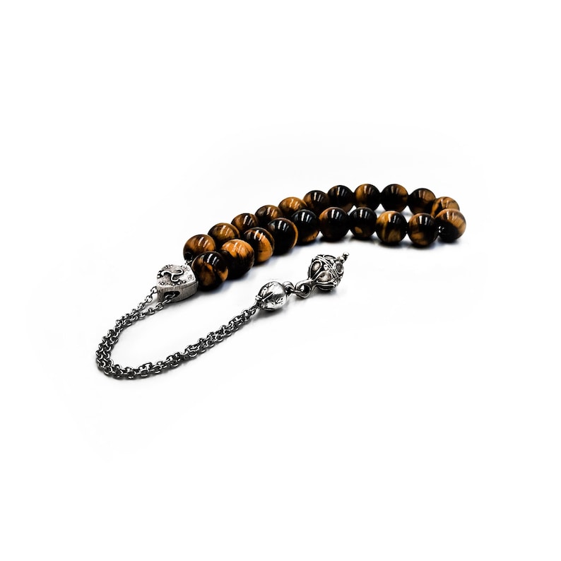 K&ouml;nnte beinhalten: Eine braune und goldene Tigerauge-Gebetskette mit silbernen Akzenten. Die Kette hat einen Quasten und einen silbernen Anh&auml;nger.